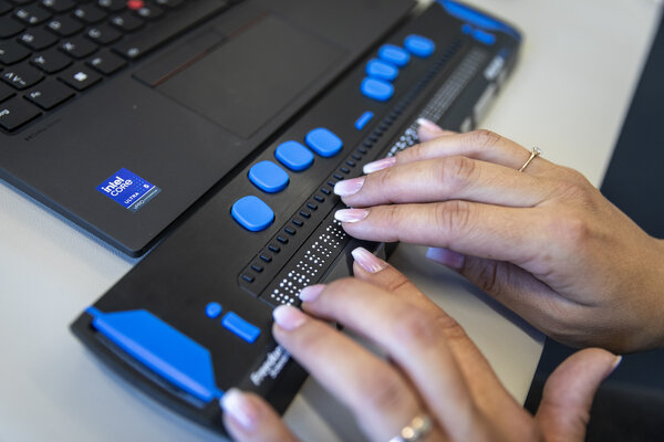 Hände lesen Text mit einer Braillezeile am Computer.